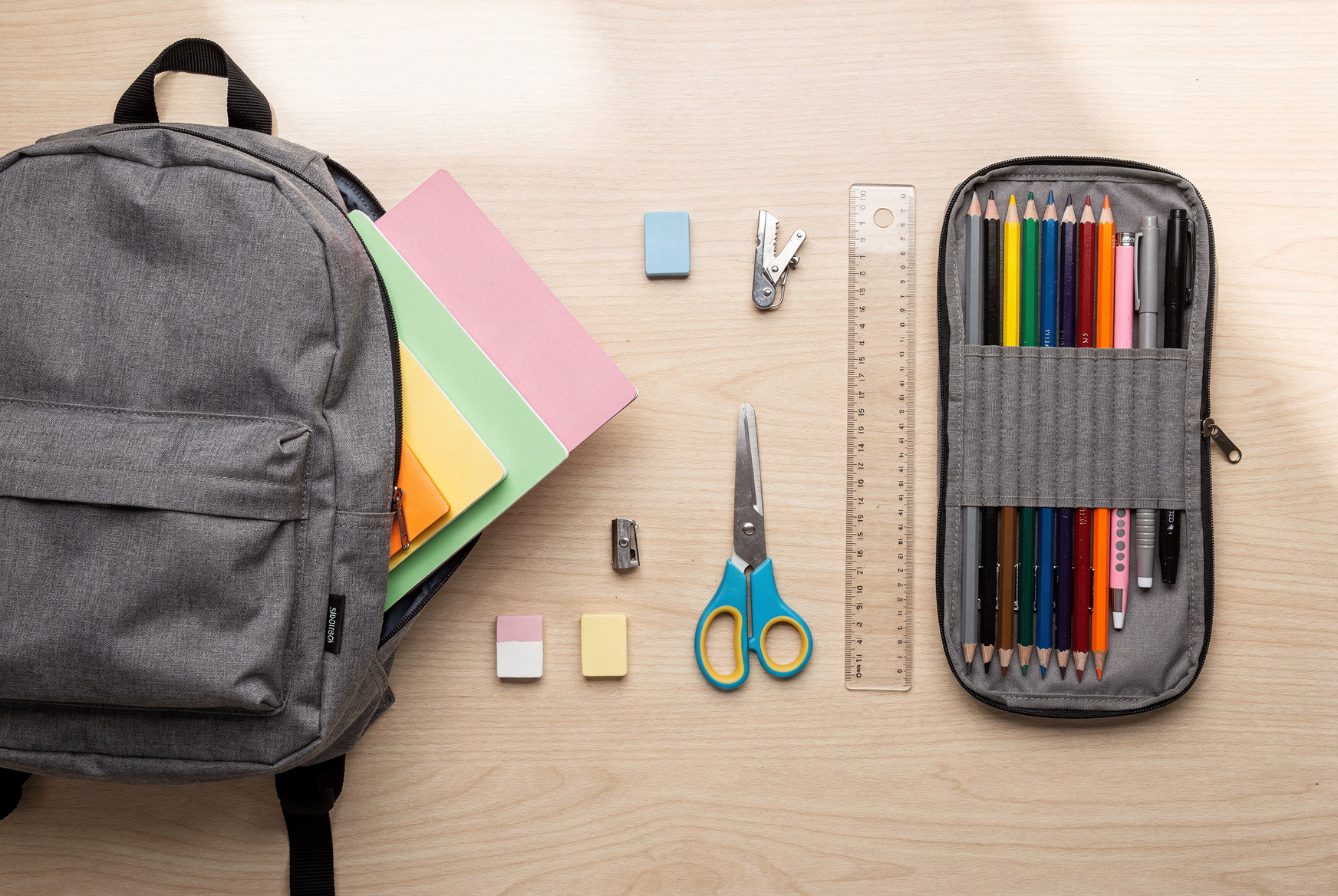 Fournitures scolaires neuves disposées sur un bureau : cartable, cahiers, trousse et crayons de couleur